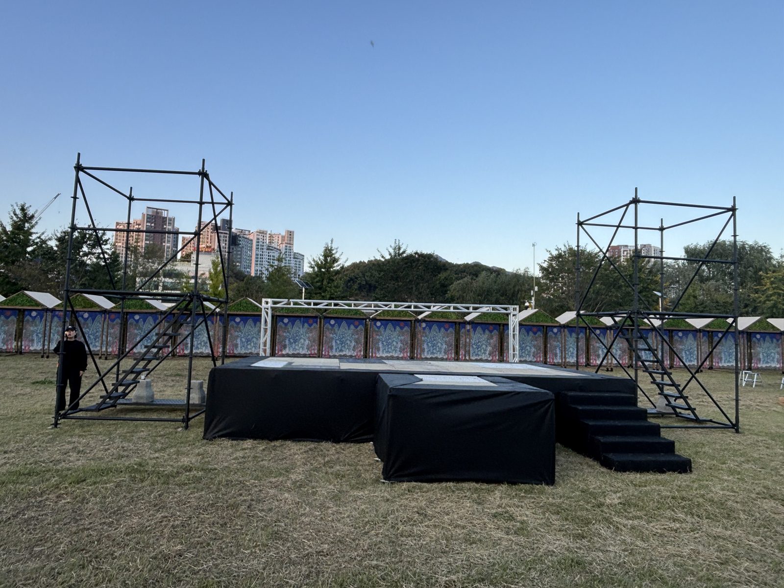 Side towers with stairs and a truss gate — outdoor park stage, Oct 2026